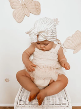 Baby in white bow turban sitting on wicker basket
