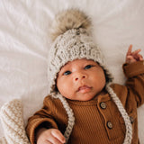 Baby wearing oatmeal cable knit bonnet - lifestyle shot showing secure fit and comfort