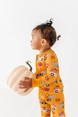 Side view of a child wearing the Let the Gourd Times Roll footie and holding a white pumpkin.