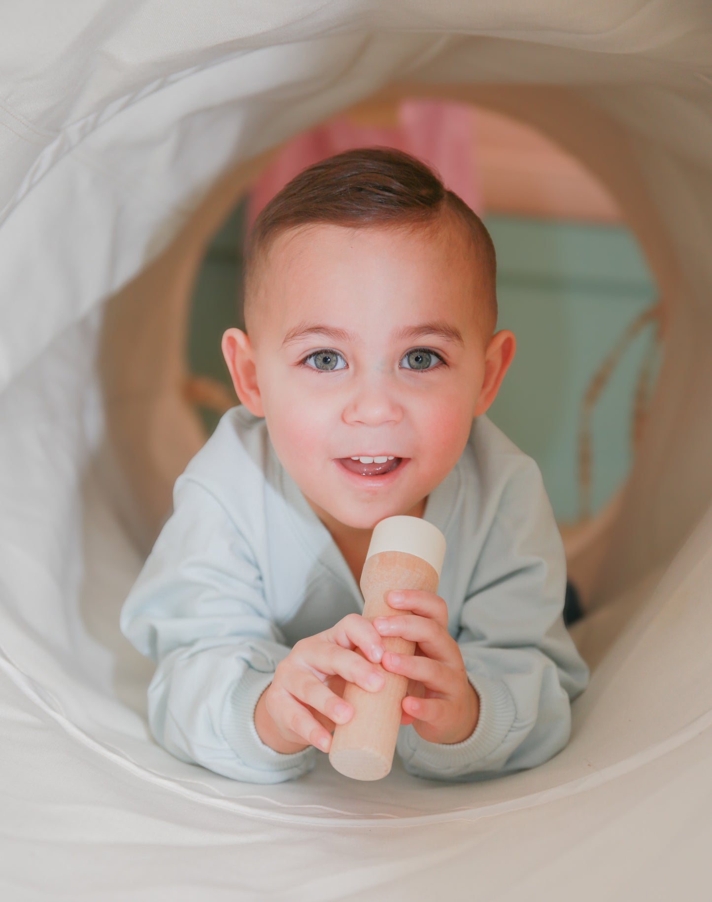 Toddler in tunnel holding wooden toy
