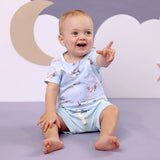 Happy baby boy in Taking Flight airplane print organic t-shirt reaching forward with cloud backdrop