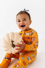 Child seated in the Let the Gourd Times Roll footie with a white pumpkin, showing the front zipper.