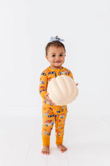 Child standing in the mustard-yellow Let the Gourd Times Roll footie, holding a white pumpkin.