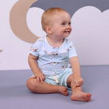 Baby boy sitting and smiling in Taking Flight organic cotton airplane print t-shirt with matching blue shorts