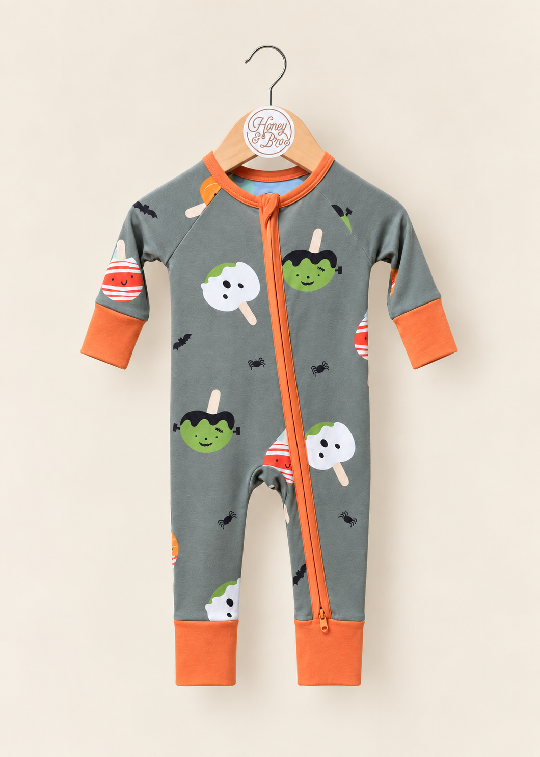 Monster Munch Zinza zippy on a hanger: muted green Halloween print with ghosts and monsters, and orange trim.