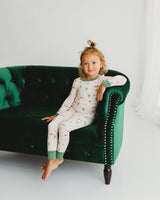 Toddler girl sitting on green velvet couch in Desert Dawn Soluna bamboo two-piece pajamas