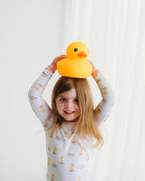 Smiling girl wearing Royal Ducklings Soluna bamboo two-piece pajamas holding yellow duck toy overhead