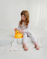 Girl sitting on white blanket wearing Royal Ducklings Soluna bamboo two-piece pajamas with duck toy