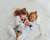 Two girls laughing in matching Harbor Dreams Soluna bamboo two-piece pajamas on white blanket