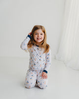 Smiling girl sitting in Harbor Dreams Soluna bamboo two-piece pajamas with sailboat print