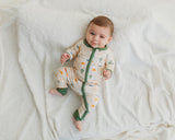 Smiling baby lying on white blanket in Desert Dawn Soluna bamboo zippy with sage cuffs