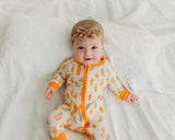 Smiling baby wearing Little Sprouts Soluna bamboo zippy with bow headband on white blanket