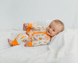 Smiling baby lounging in Little Sprouts Soluna bamboo zippy with orange cuffs on white blanket