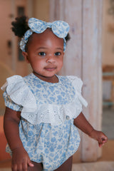 Toddler girl standing in blue floral lace romper with matching headband - smiling portrait