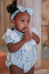 Toddler girl in blue floral romper with eyelet lace collar and matching bow headband - close up