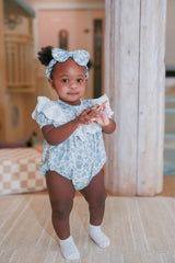 Toddler girl standing in blue floral lace romper with matching headband - full body lifestyle shot