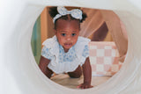 Toddler girl crawling through play tunnel in blue floral lace romper with matching headband