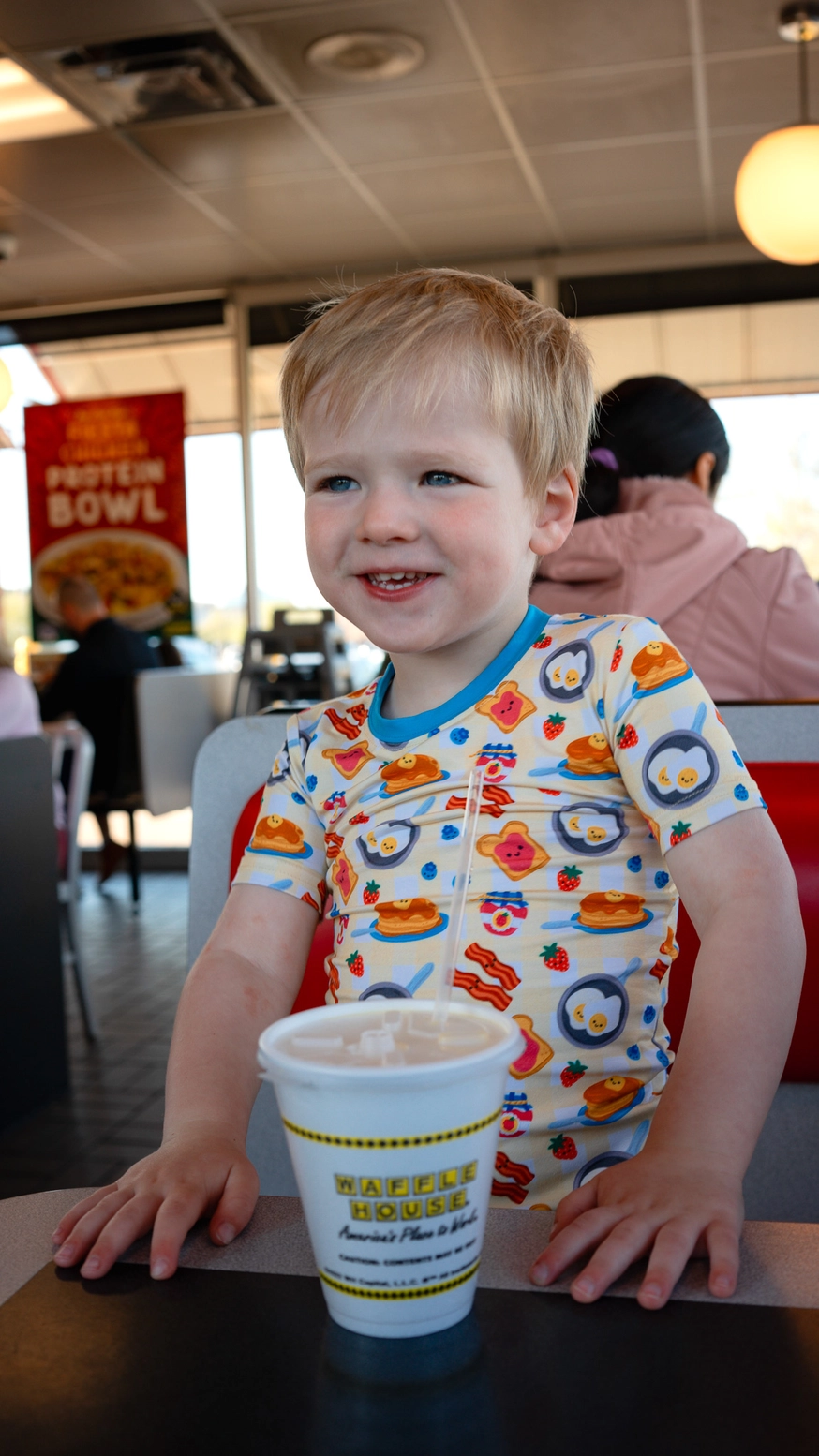 Smiling child wearing Breakfast Buddies bamboo pajamas at brunch table