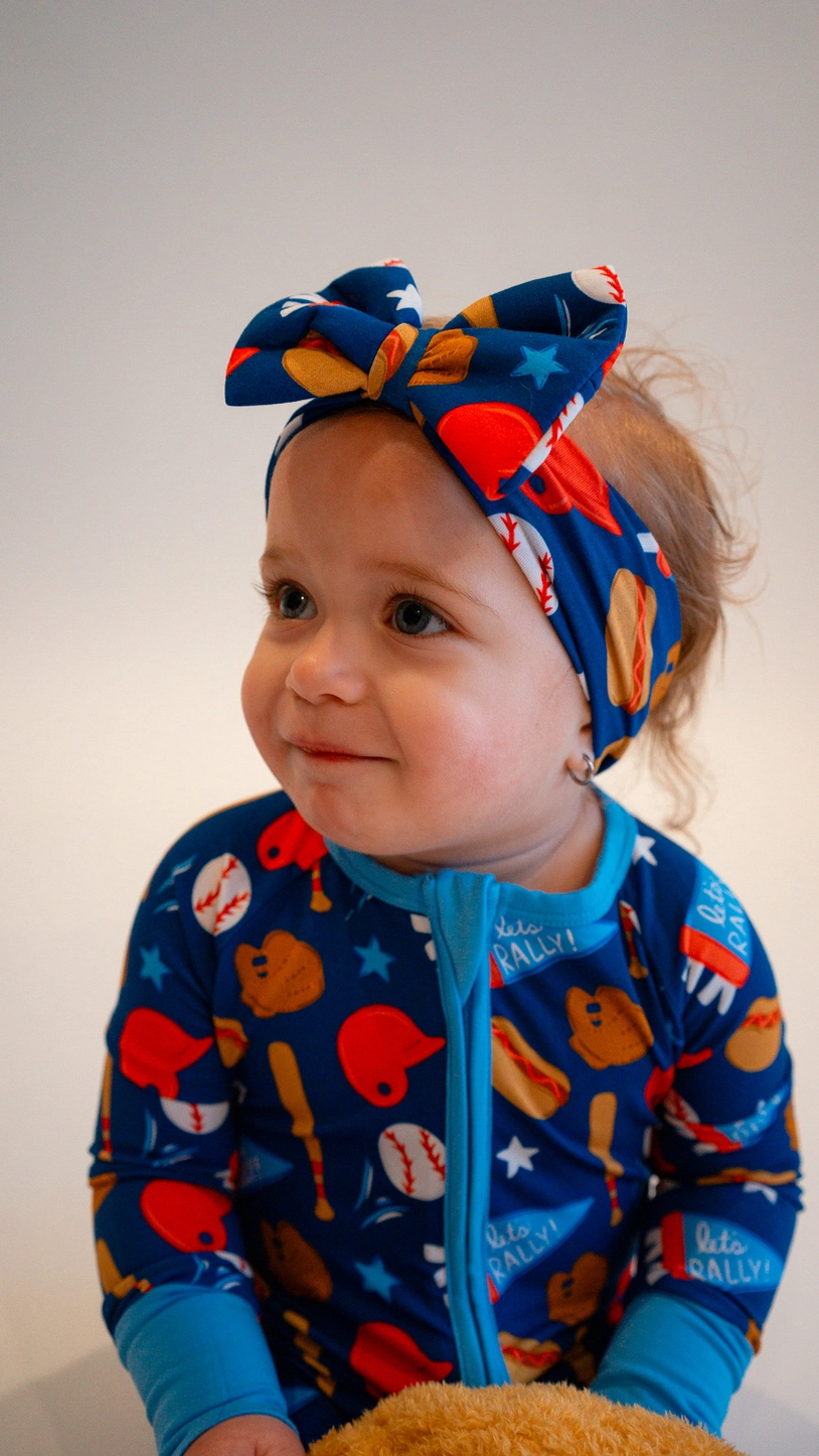 Baby girl with matching baseball bow headband wearing Baseball Bamboo Zippy Pajamas side profile