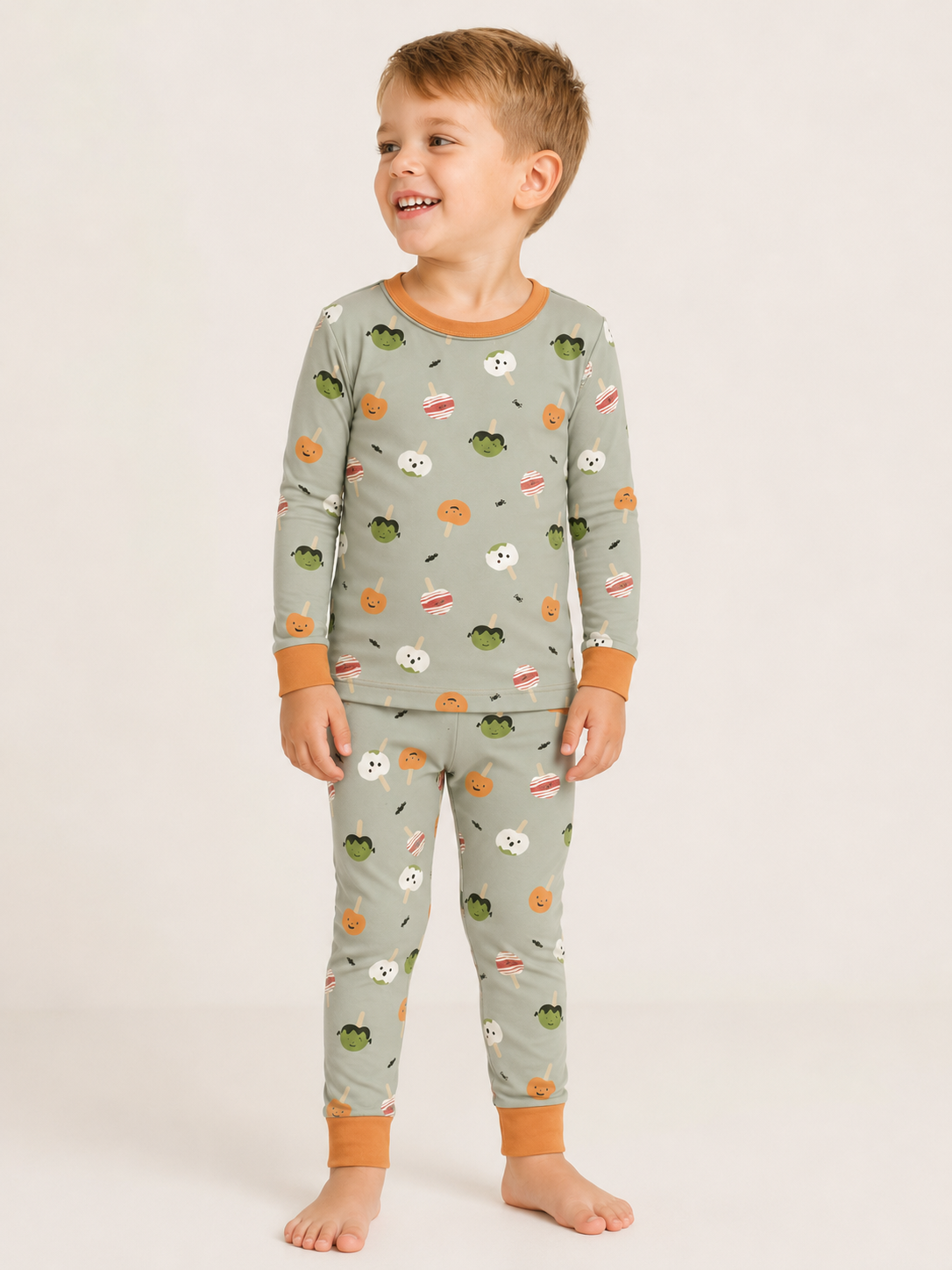 Toddler wearing the Monster Munch Zinza two-piece pajama set with Halloween treats on sage and orange trim