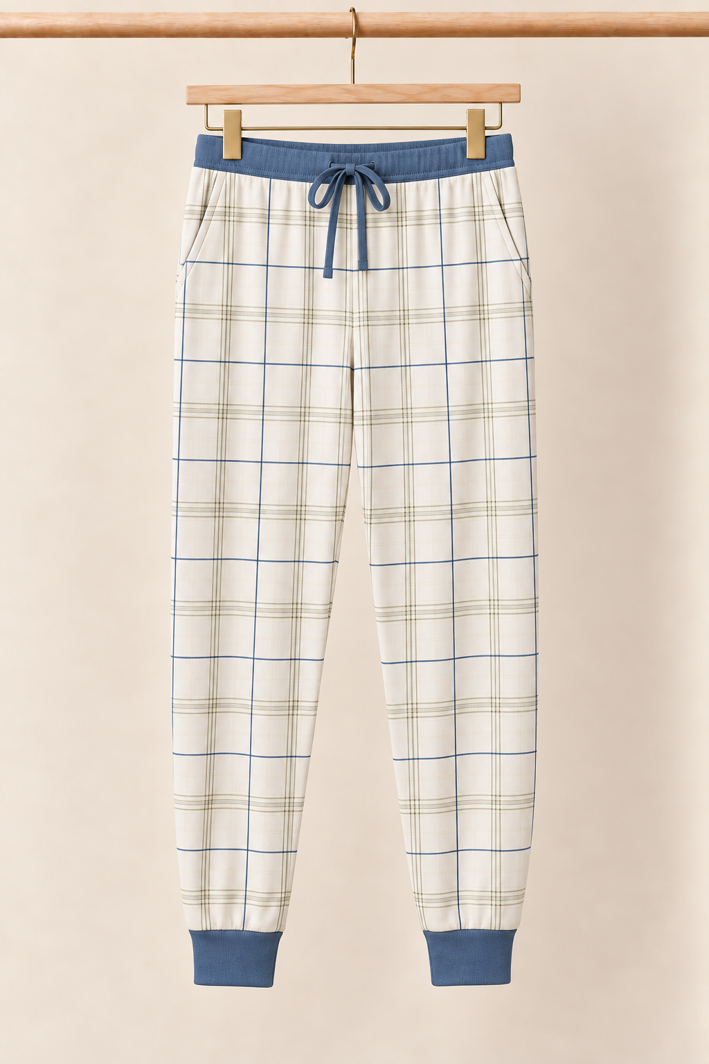 Fireside Windowpane ivory plaid adult pajama joggers with slate blue drawstring and cuffs on a wooden clip hanger against a creamy background