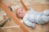 Baby in blue and white gingham romper through wooden play gym