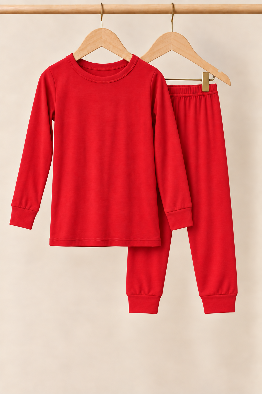 Holly Berry solid red toddler two-piece pajamas on wooden hangers against a creamy background