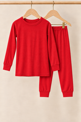 Holly Berry solid red toddler two-piece pajamas on wooden hangers against a creamy background