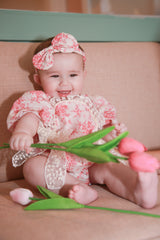 Baby girl in pink rose floral romper with matching headband and lace detail - sitting with pink tulips