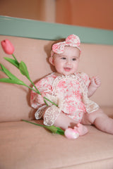 Baby girl smiling in pink rose print romper with matching bow headband holding pink tulip