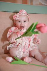 Baby girl in pink rose romper with matching headband reaching for pink tulips - close up