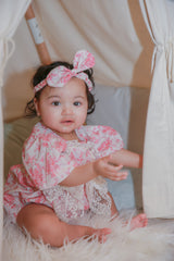 Toddler girl in pink rose romper with matching headband sitting in teepee tent on faux fur