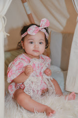 Toddler girl portrait in pink rose floral romper with lace detail and matching bow headband