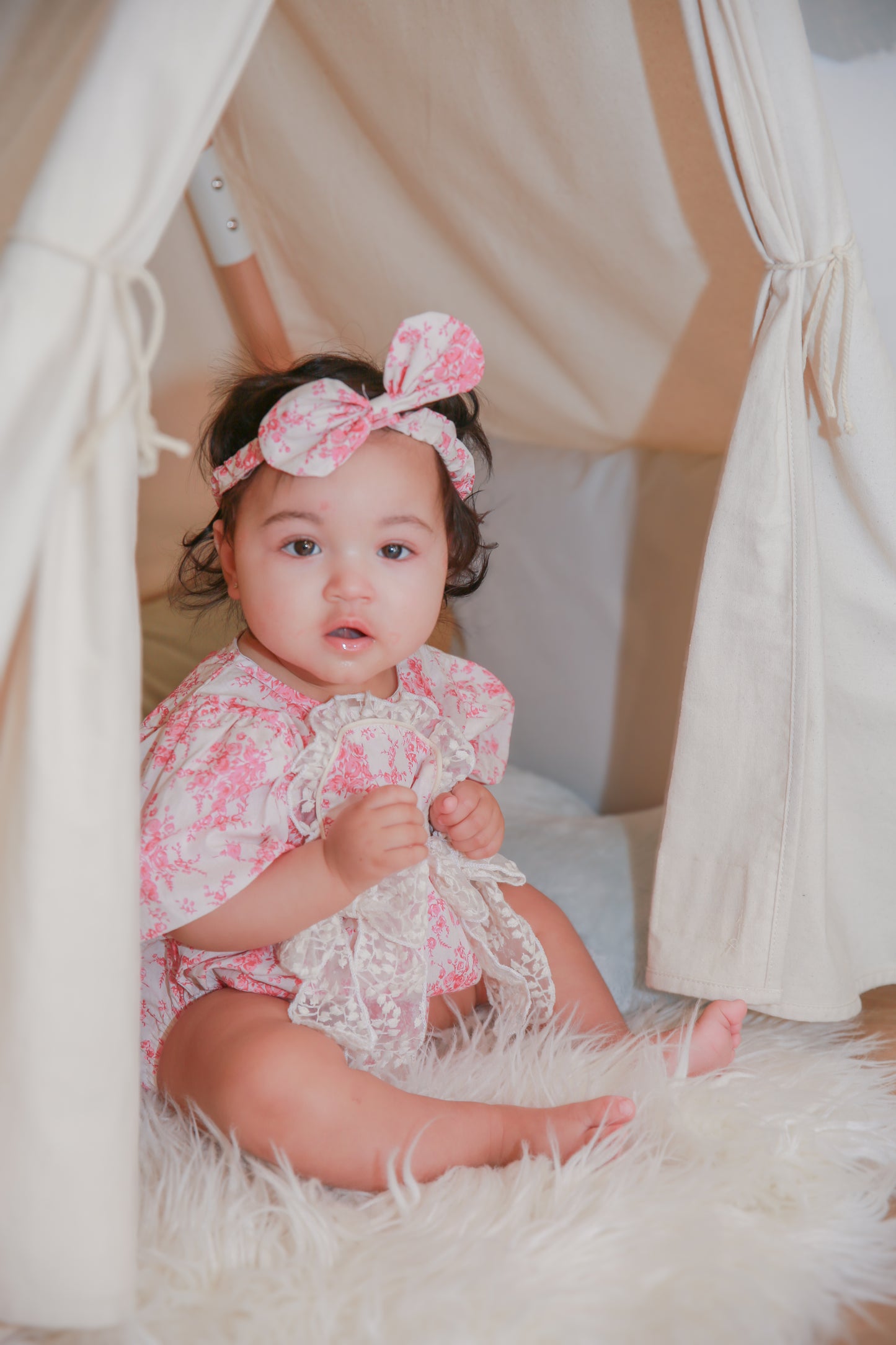 Toddler girl in pink rose romper sitting in boho teepee tent - lifestyle shot