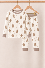 Winter Gingerbread Zinza™ Kids Two-Piece Pajama Set on wooden hangers against a warm cream background